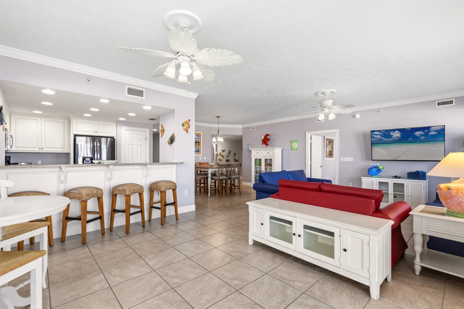 Relax in your coastal-themed living space with ocean-view TV, full kitchen, and tropical ceiling fans creating the perfect beach getaway atmosphere.