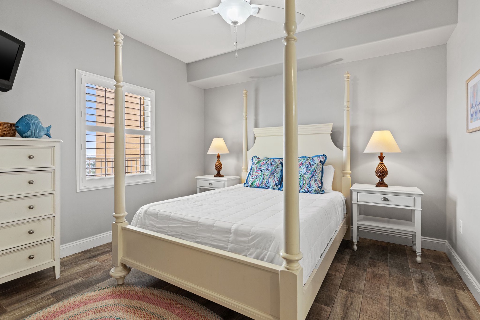 Your coastal-style bedroom features a classic four-poster bed with vibrant accent pillows, nightstands with warm lamps, and a ceiling fan to keep you comfortable all night long.