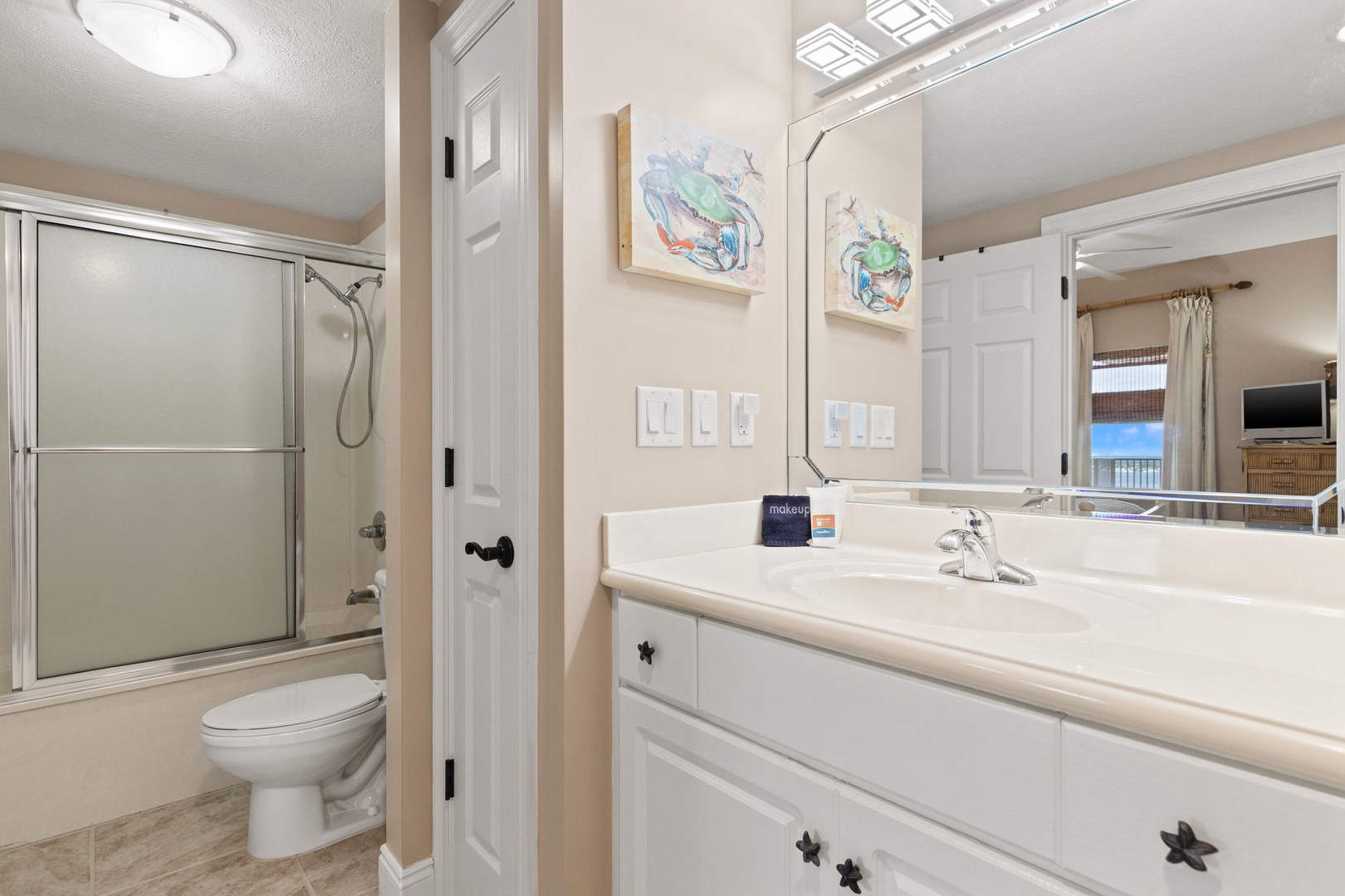 Freshen up in your coastal-inspired bathroom featuring a glass-enclosed shower and bright vanity space, beautifully accented with beachy artwork that brings the shore indoors.