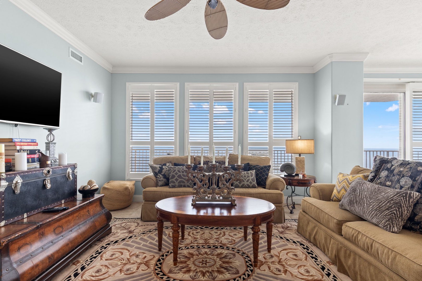 Relax in your coastal living room with elegant furnishings, a ceiling fan, and stunning ocean views through plantation shutters. Perfect for unwinding after beach days.