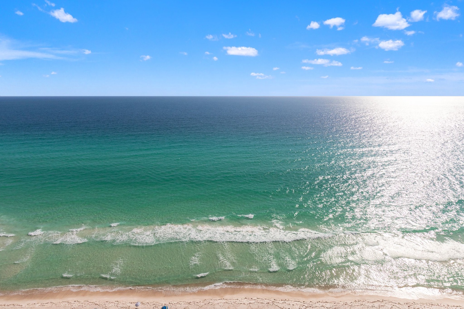 Pristine beach with emerald waters and white sand stretches endlessly under brilliant blue skies dotted with fluffy clouds.