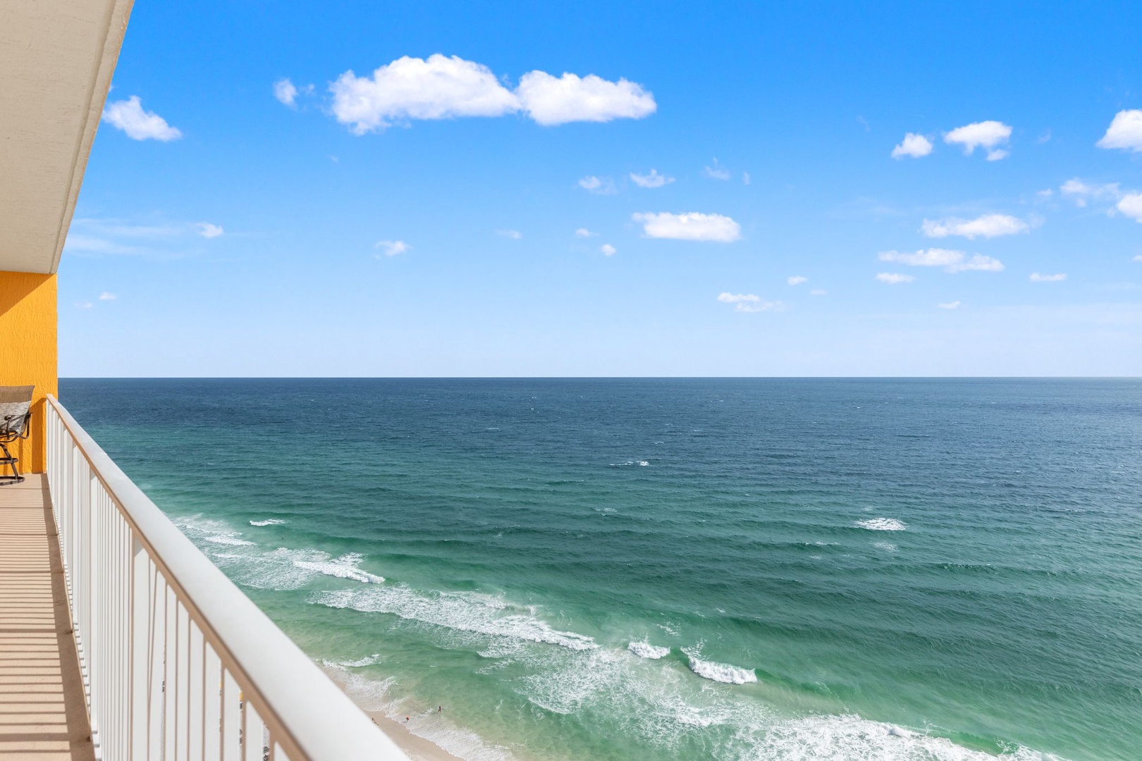 The property offers an oceanfront balcony with a stunning view of the emerald-green Gulf waters and gentle waves rolling onto the sandy shore below.