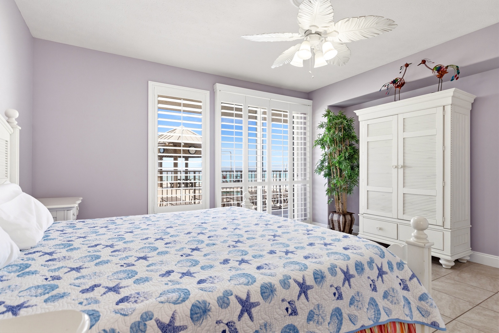 Wake up to ocean breezes in your serene coastal bedroom, where soft lavender walls and tropical ceiling fan create the perfect beach retreat sanctuary.