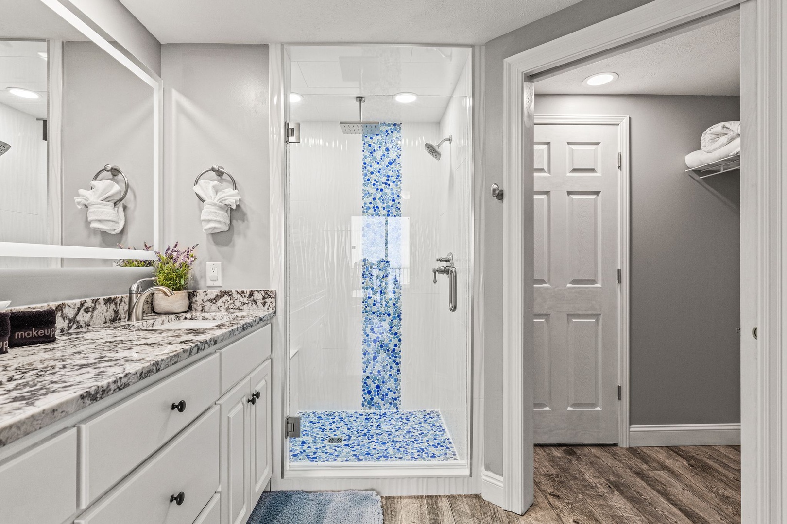 Step into your spa-inspired bathroom, where blue mosaic tiles add coastal charm to the walk-in shower. Fresh towels and granite countertops create a refined, welcoming retreat.