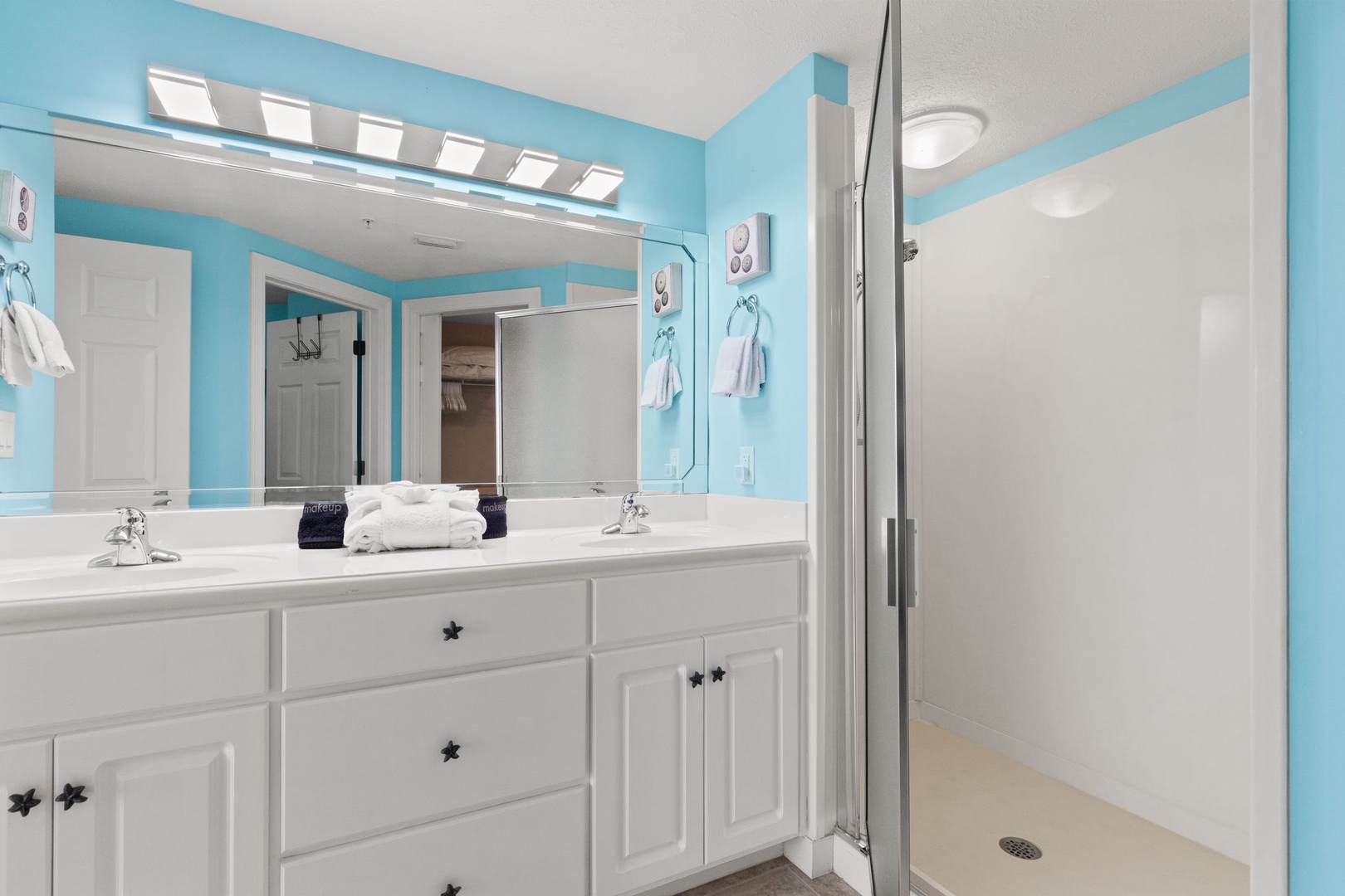 Your spacious bathroom features dual vanities, a generous walk-in shower, and cheerful coastal-inspired décor that brightens every morning routine.