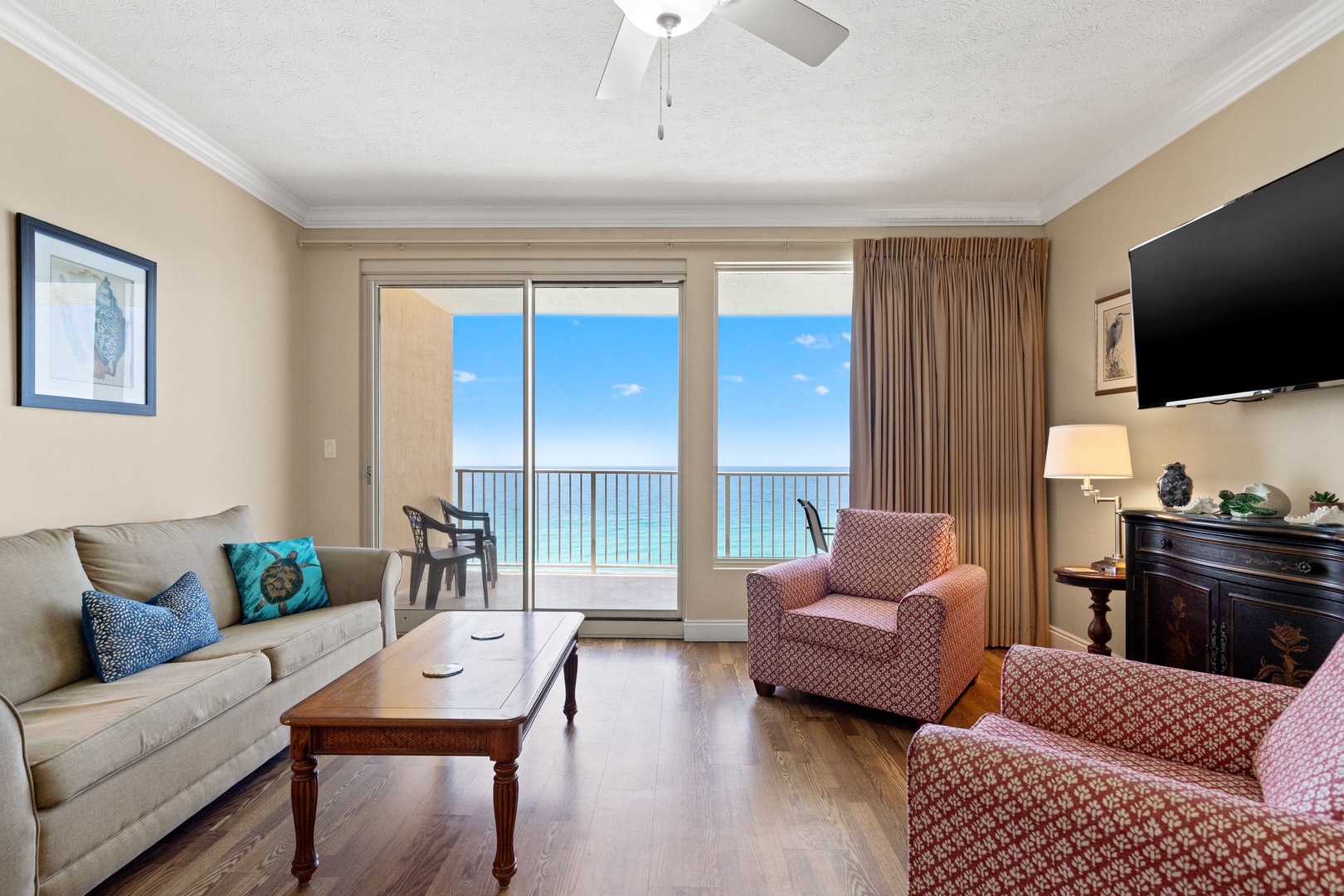 Relax in your inviting living room with stunning ocean views through floor-to-ceiling glass doors. Comfortable seating, warm wood floors, and a gentle ceiling fan breeze set the tone for your perfect coastal getaway.
