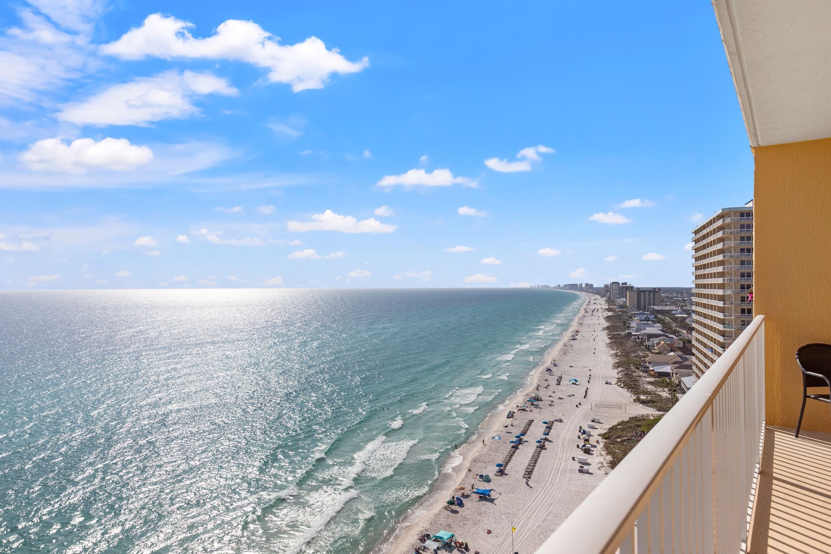 Expansive beachfront with white sand stretching along turquoise waters, framed by coastal high-rises. A sunny day view of the surrounding area from an elevated perspective.
