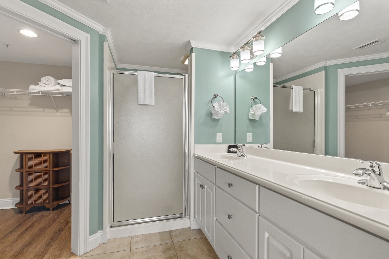 Refresh in your spacious bathroom featuring dual sinks, elegant lighting, and a glass-enclosed shower with soft green accents.