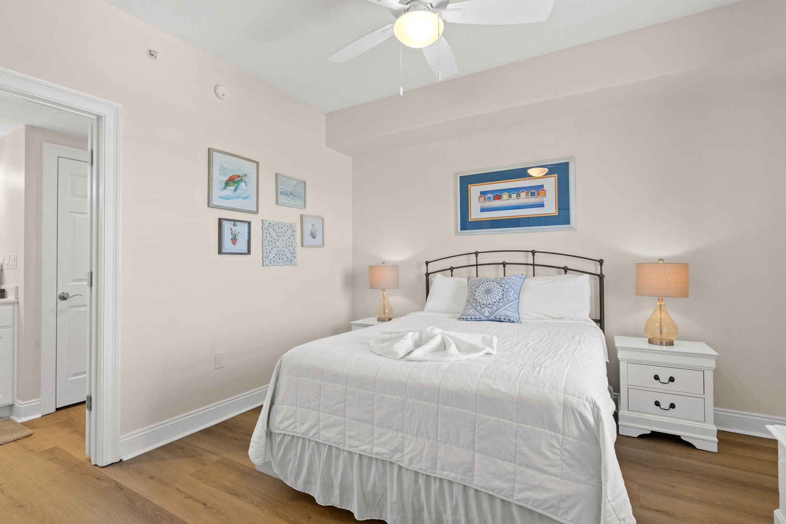 Relax in your cozy bedroom featuring crisp white linens, coastal artwork, and warm bedside lighting for peaceful nights.