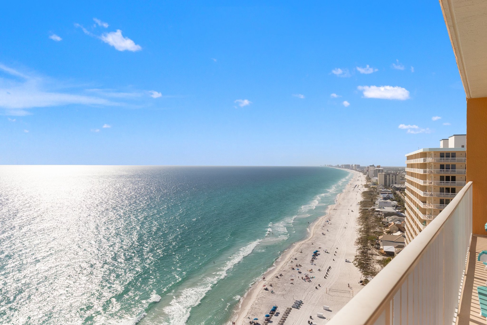 Stunning beachfront stretches endlessly along pristine turquoise waters, with modern high-rise buildings dotting the coastal horizon under brilliant blue skies.