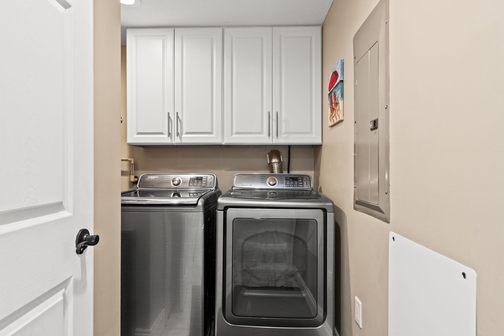 Enjoy the convenience of your own washer and dryer tucked into this dedicated laundry space. White cabinetry above provides ample storage for detergents and linens, making it easy to keep fresh clothes ready for your beach adventures.