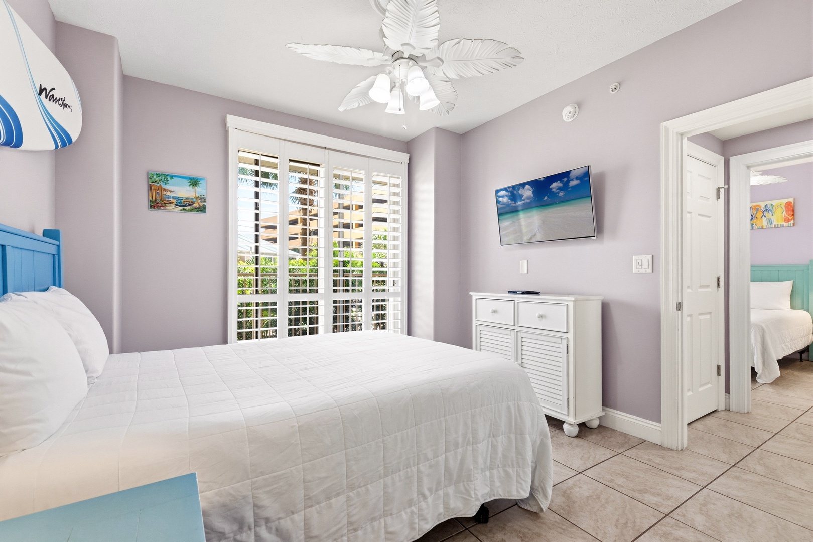 Drift off to sleep in your serene bedroom with tropical ceiling fan, flat-screen TV, and peaceful coastal decor creating the perfect retreat.