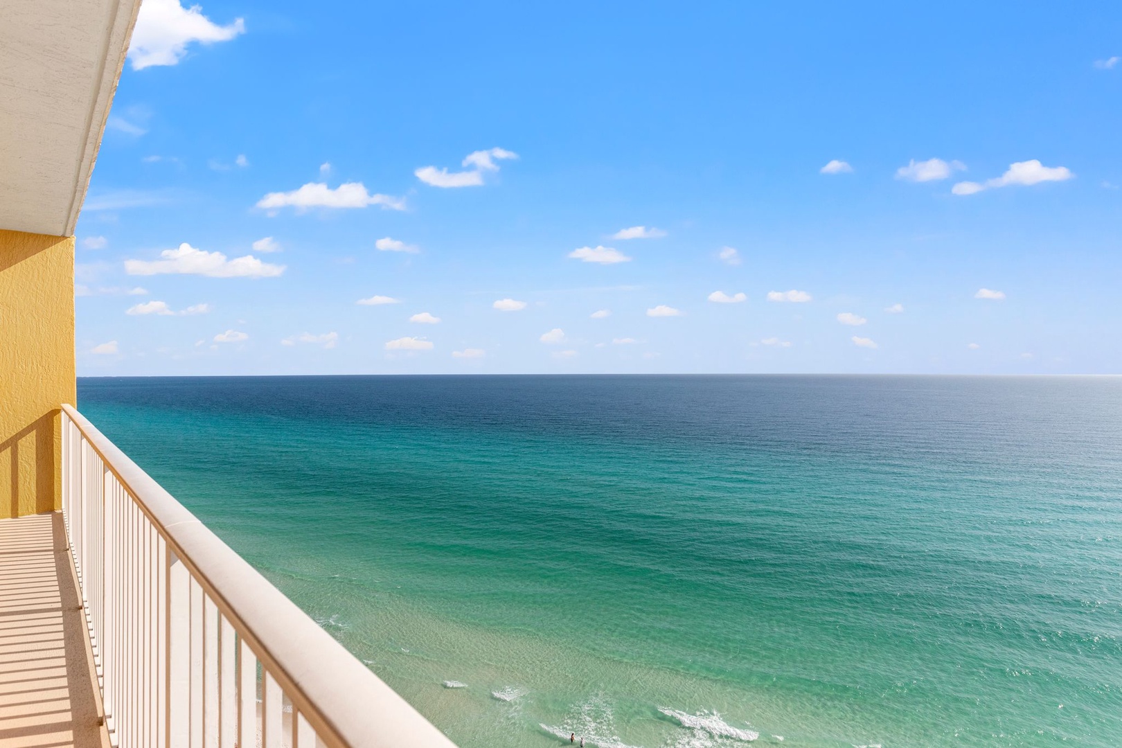 Stunning beachfront view showcases turquoise waters stretching to the horizon under a bright blue sky dotted with soft clouds. The property offers direct access to pristine coastal beauty.