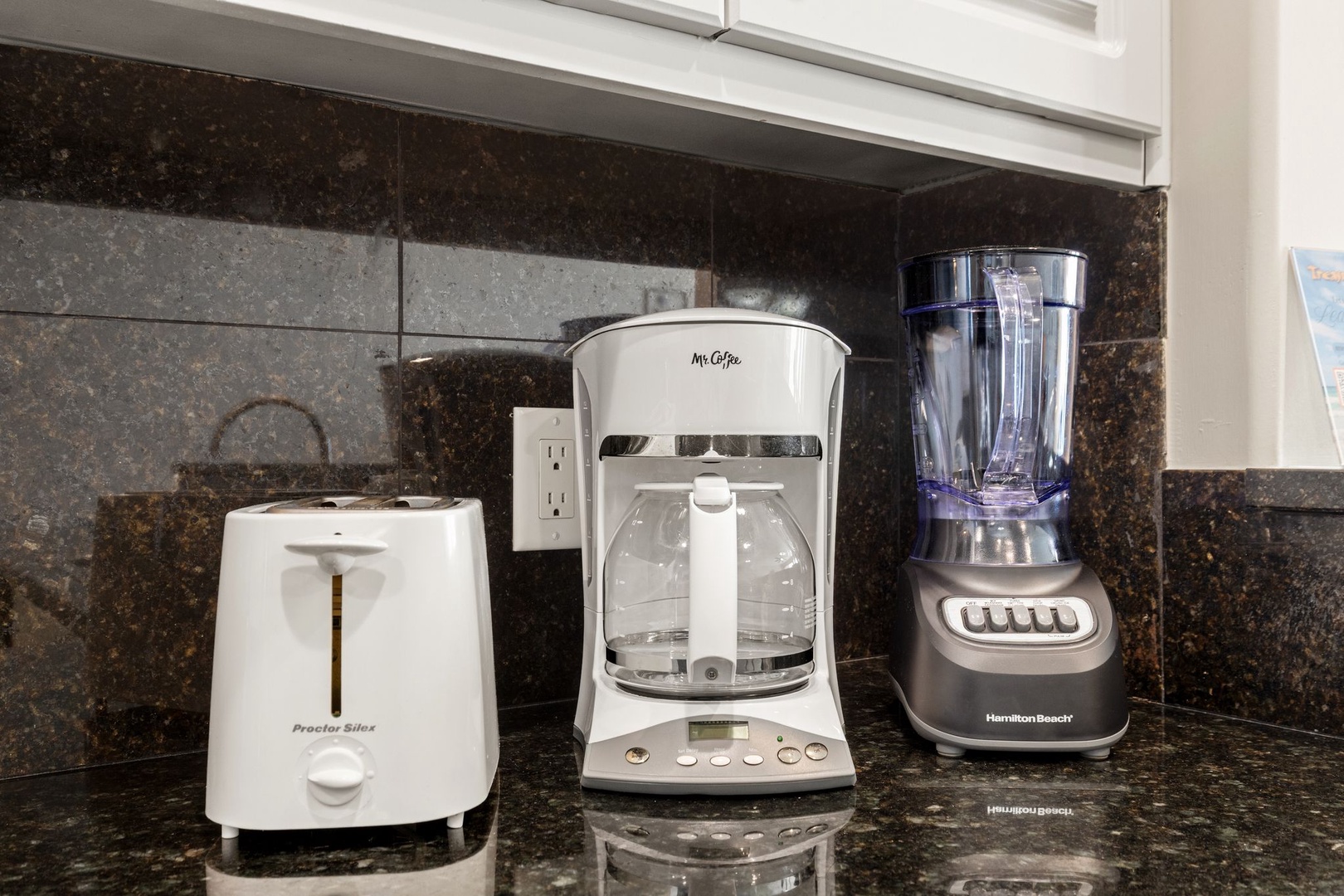 Wake up to fresh coffee and smoothies with this well-equipped kitchen counter featuring a coffee maker, toaster, and blender for your convenience.