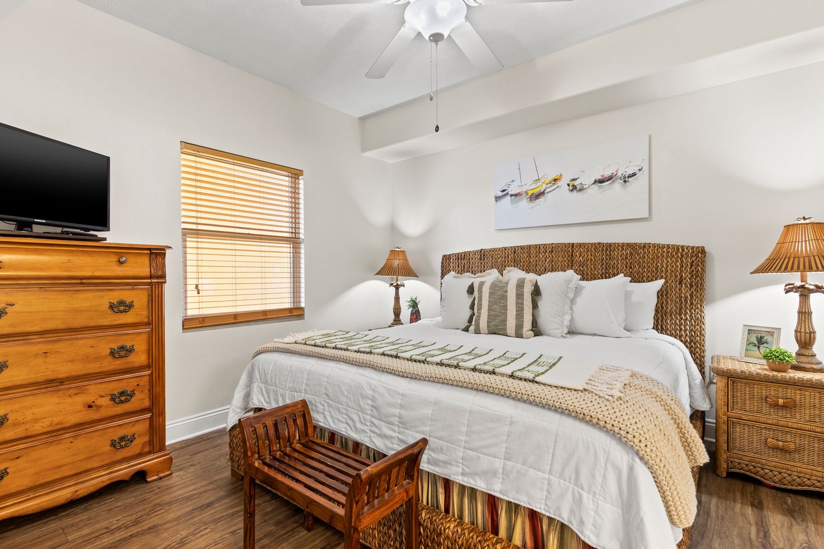 You'll find peaceful rest in this coastal-inspired bedroom with plush bedding, woven textures, and soothing beach artwork. Morning light filters through plantation blinds while ceiling fan keeps you comfortable year-round.