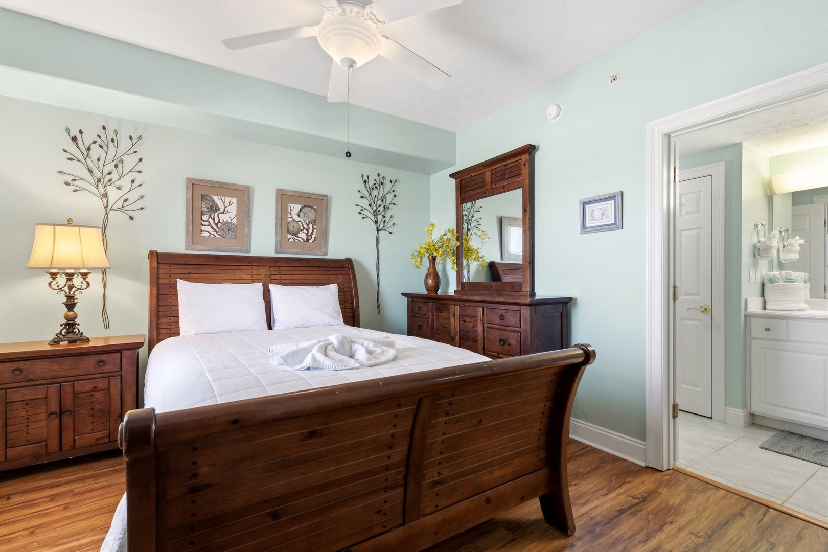 Relax in your peaceful bedroom featuring warm wood furnishings, soft linens, and a charming ceiling fan for ultimate comfort.