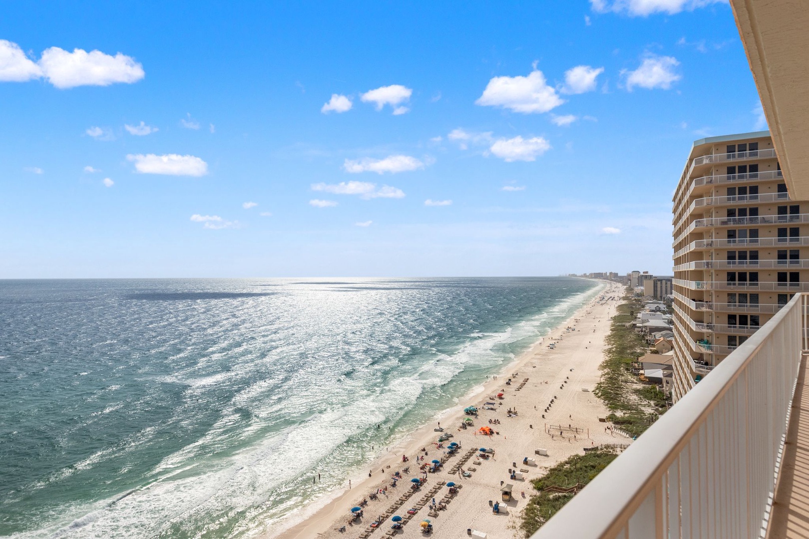 This beachfront property offers stunning views of the pristine coastline, with white sand stretching along turquoise waters and neighboring buildings visible along the shore.