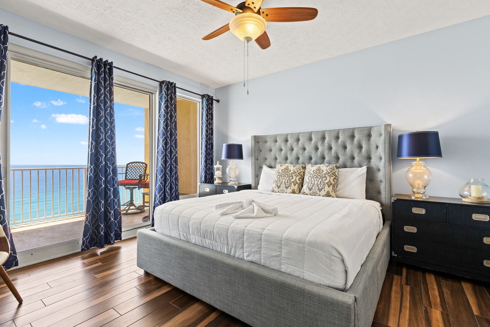 Wake up to breathtaking ocean views framed by sliding glass doors that open onto your private balcony. This elegant bedroom features a plush tufted bed, stylish furnishings, and warm wood floors—your peaceful seaside retreat.