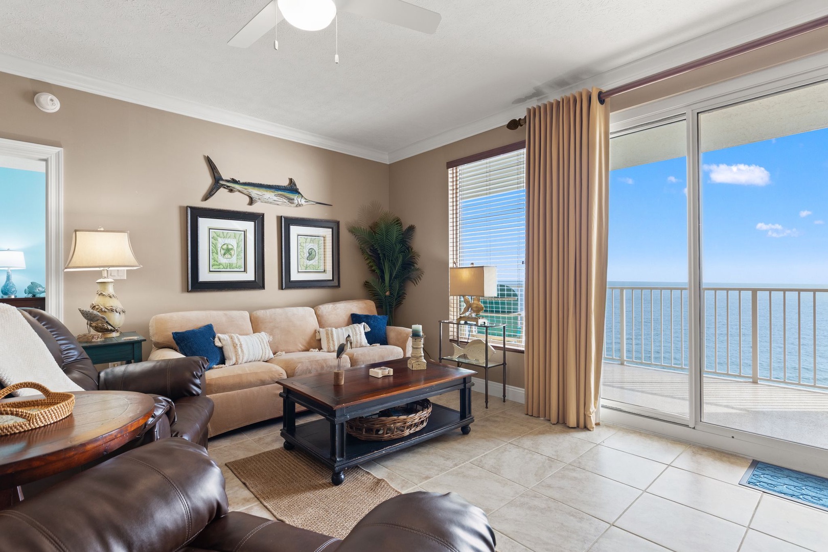 Step into your coastal haven where ocean views stretch endlessly beyond the spacious balcony. Relax in the bright, airy living room with comfortable seating, nautical touches, and calming blue accents that invite effortless unwinding.