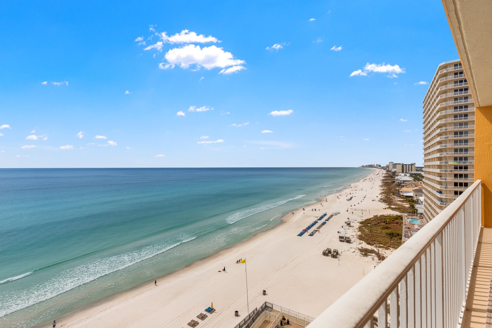 Stunning beachfront vista stretches endlessly along pristine white sand, with crystal-clear emerald waters and neighboring resort buildings creating the perfect coastal setting.