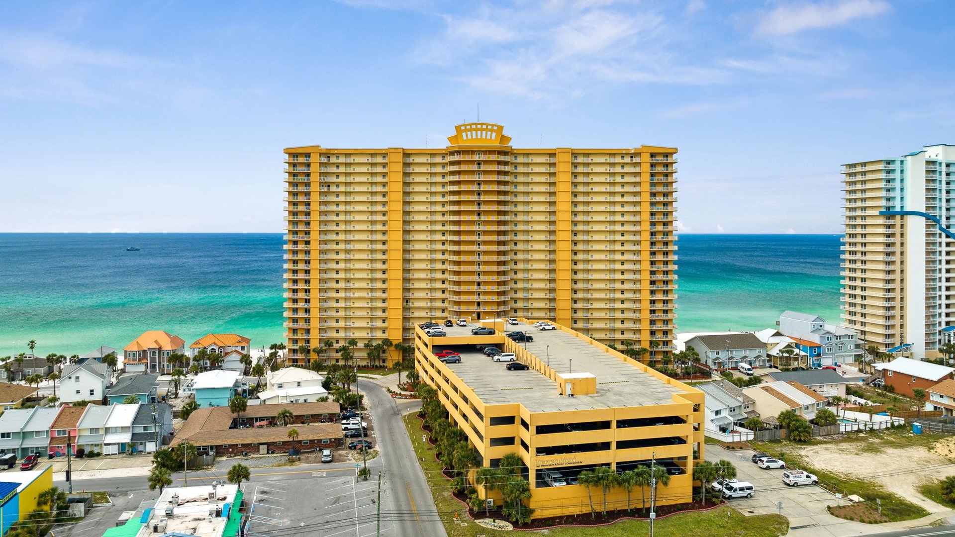Oceanfront high-rise building with parking garage situated near beautiful turquoise waters and beachfront neighborhood.