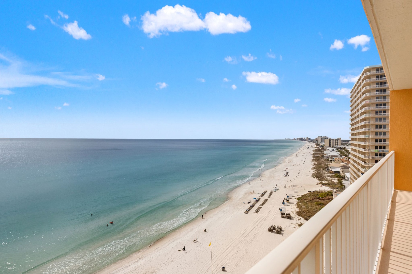 Panoramic beachfront view showcasing pristine sandy shores, turquoise waters, and coastal high-rise buildings under blue skies with scattered clouds.