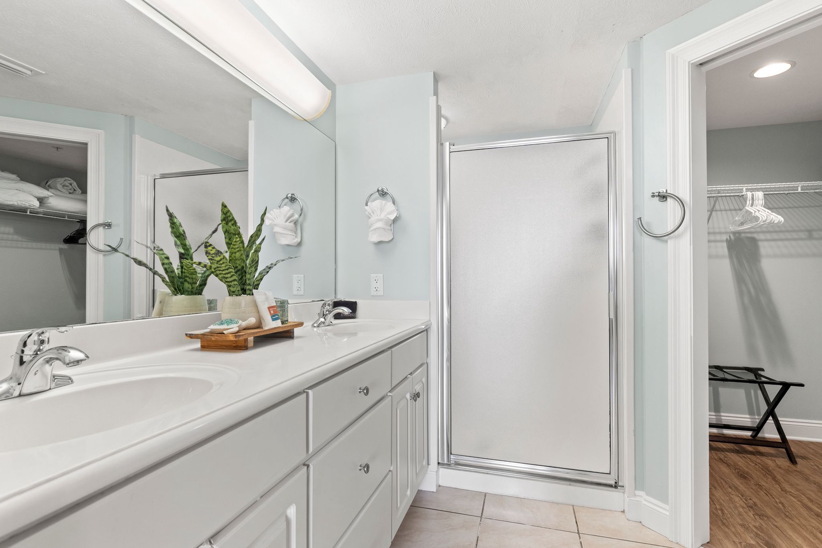Refresh in your spa-like bathroom with soft blue walls, a spacious vanity, and a sleek walk-in shower. Plush towels and a touch of greenery create a calm, inviting start to your day.