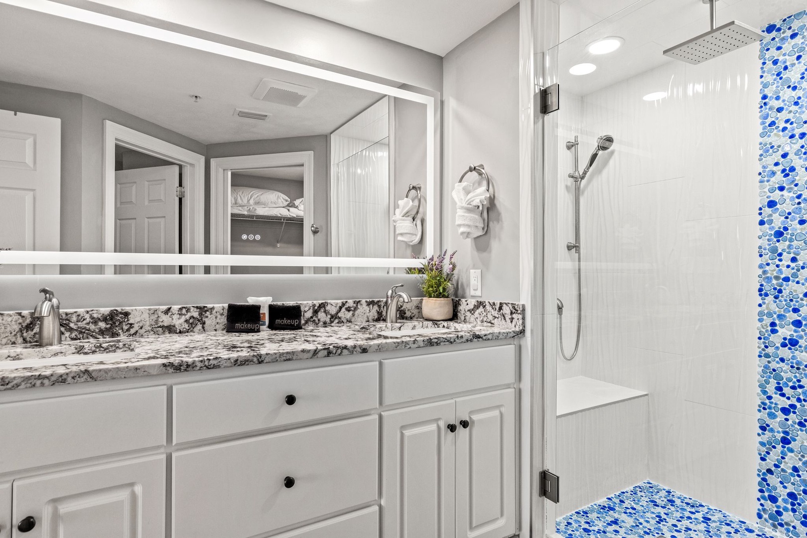 Step into your private spa-like bathroom featuring a rainfall shower, granite countertops, and coastal-inspired mosaic tilework. Fresh towels and thoughtful amenities await your arrival.