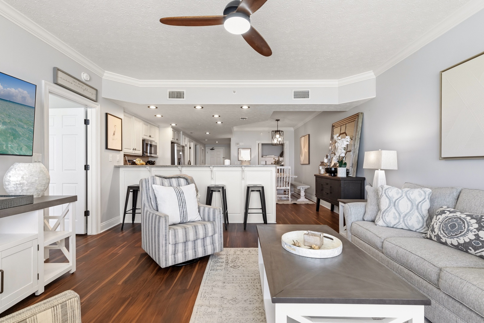 Relax in your elegant open-concept living space with modern kitchen, coastal décor, and rich hardwood floors beneath soaring ceilings.