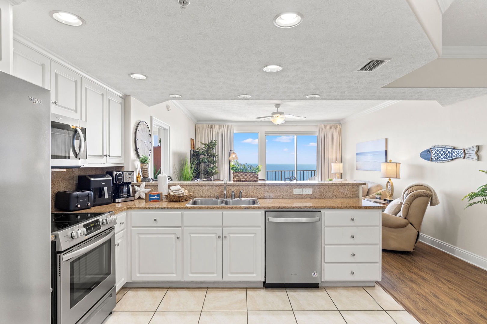 This open-concept kitchen flows seamlessly into the living space, with white cabinetry, stainless steel appliances, and granite countertops—all framed by stunning ocean views that you'll enjoy while cooking.