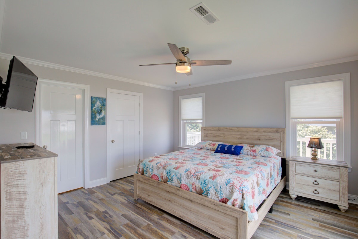 A bedroom with a bed, a ceiling fan, a nightstand, a TV, and a window.