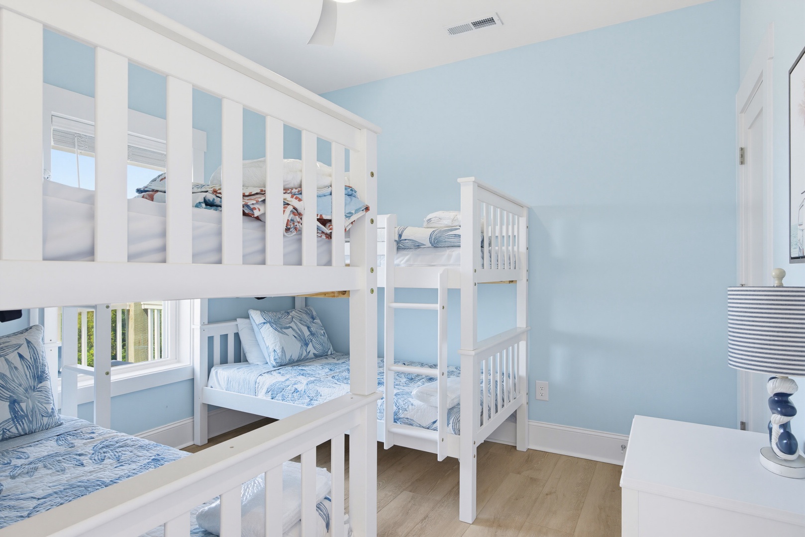 Perfect for kids or groups, this bright coastal bedroom features crisp white bunk beds dressed in soft blue linens. A window lets in natural light, while the calming blue walls create a serene, beachy retreat for your family to rest and recharge.