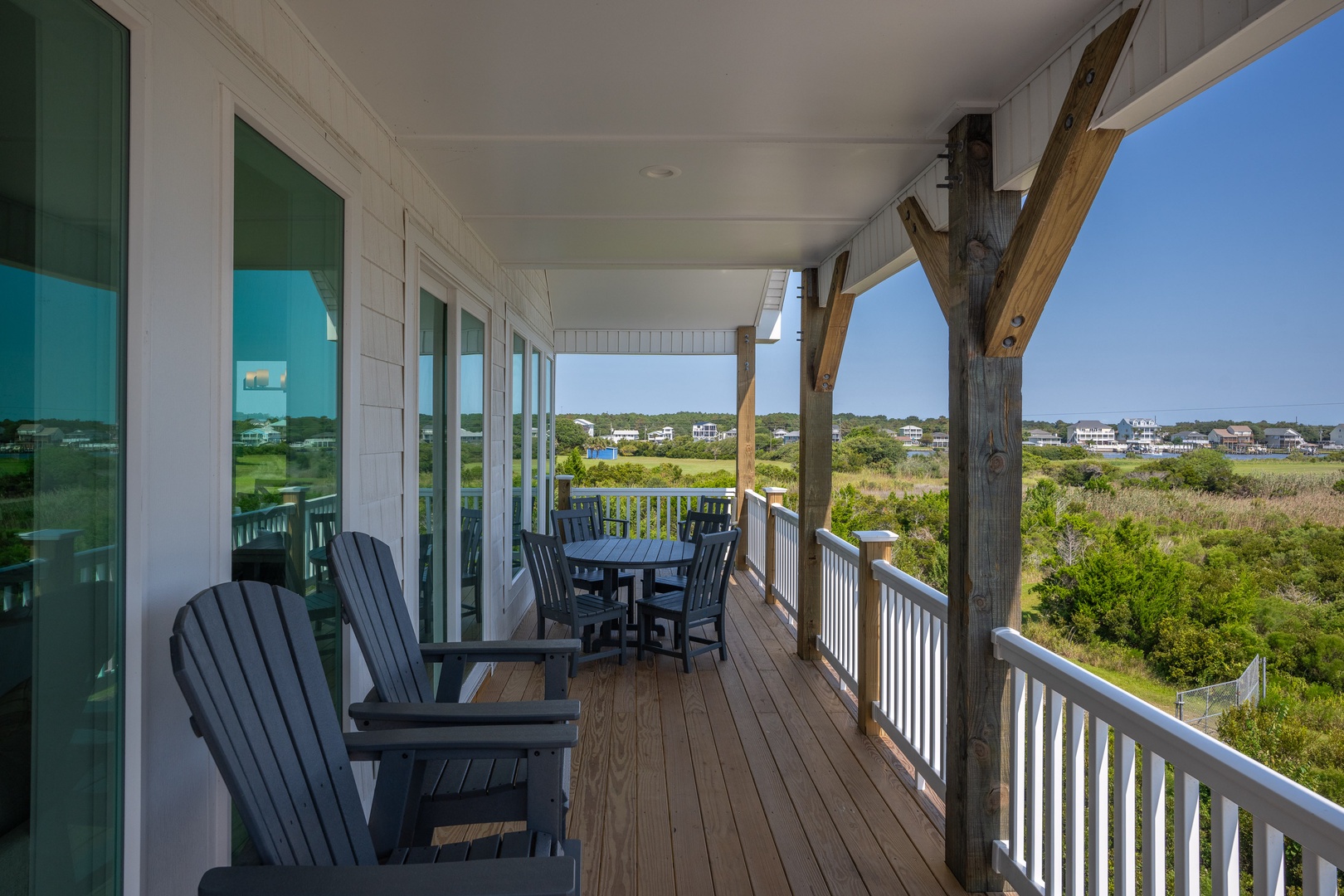 This covered porch features sweeping views over coastal marshland and distant homes. Comfortable Adirondack chairs and a dining table make it ideal for outdoor relaxation and al fresco meals.