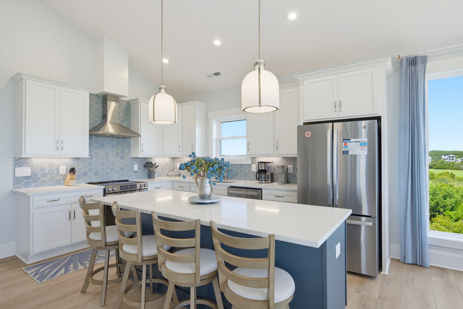 Gather around the bright island in this open coastal kitchen, where white cabinetry and calming blue accents create a welcoming space for your morning coffee or meal prep.