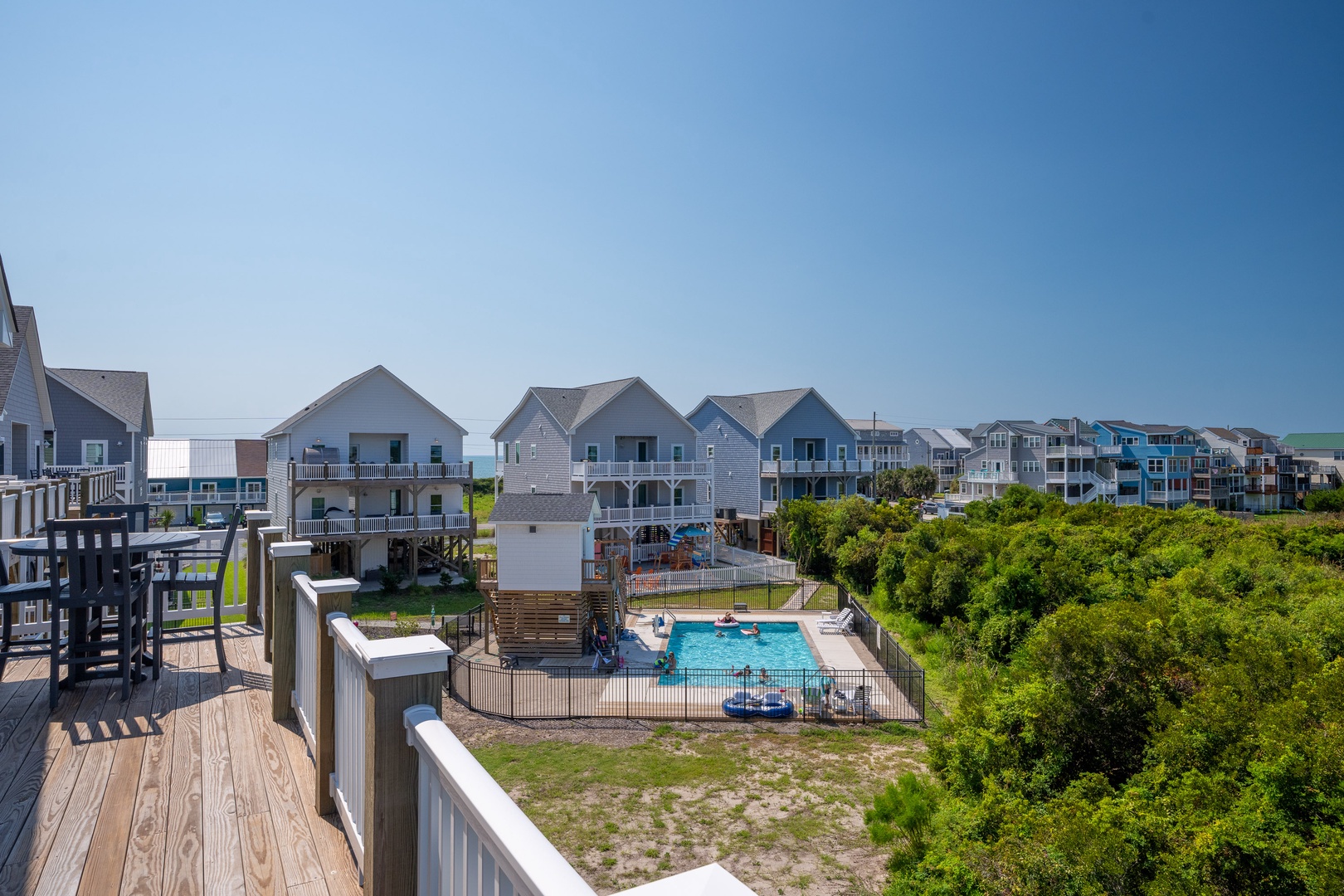 A coastal community with beach houses, a sparkling communal pool, and lush greenery, all under a clear blue sky near the ocean.