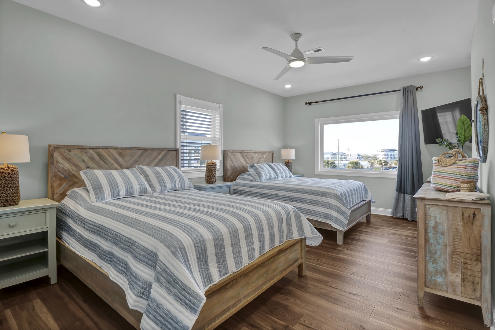 Unwind in your serene coastal bedroom, where two comfortable beds await you under a soothing blue ceiling fan. Soft striped linens and warm wood tones create a calming retreat after a day at the beach.