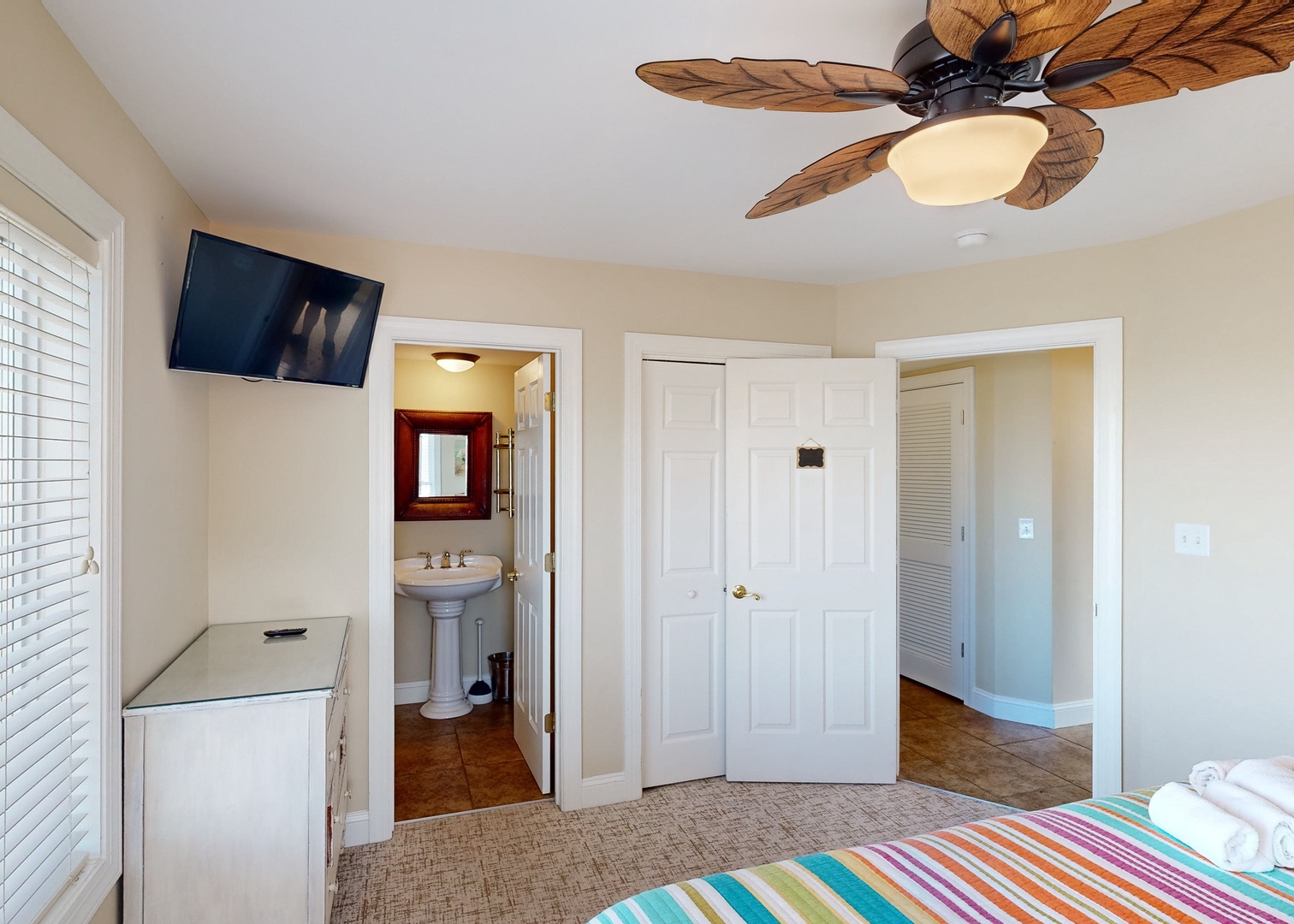 Your bright, beachy bedroom features a tropical ceiling fan overhead and colorful striped bedding, with an ensuite bathroom and closet conveniently nearby for your ultimate comfort.