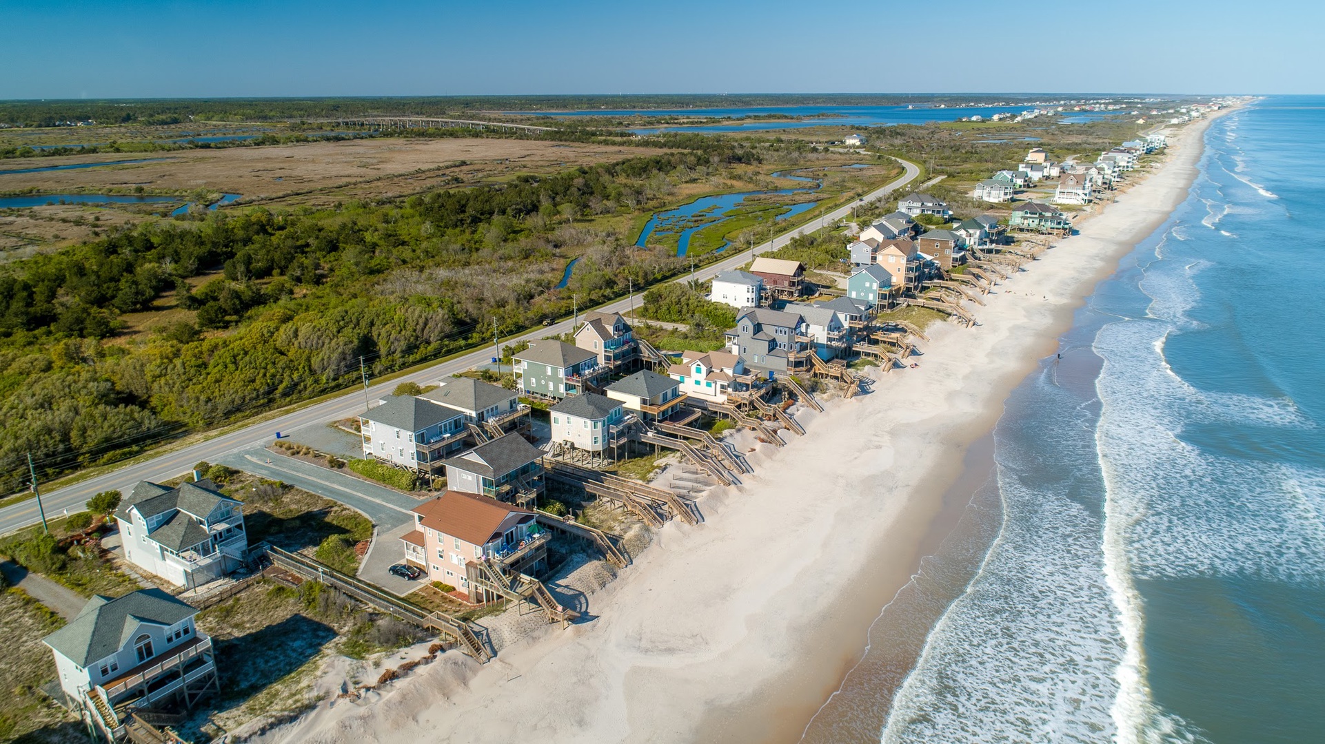 Aerial view of beachfront vacation rentals lining a pristine stretch of coastline, surrounded by natural marshlands and coastal vegetation.