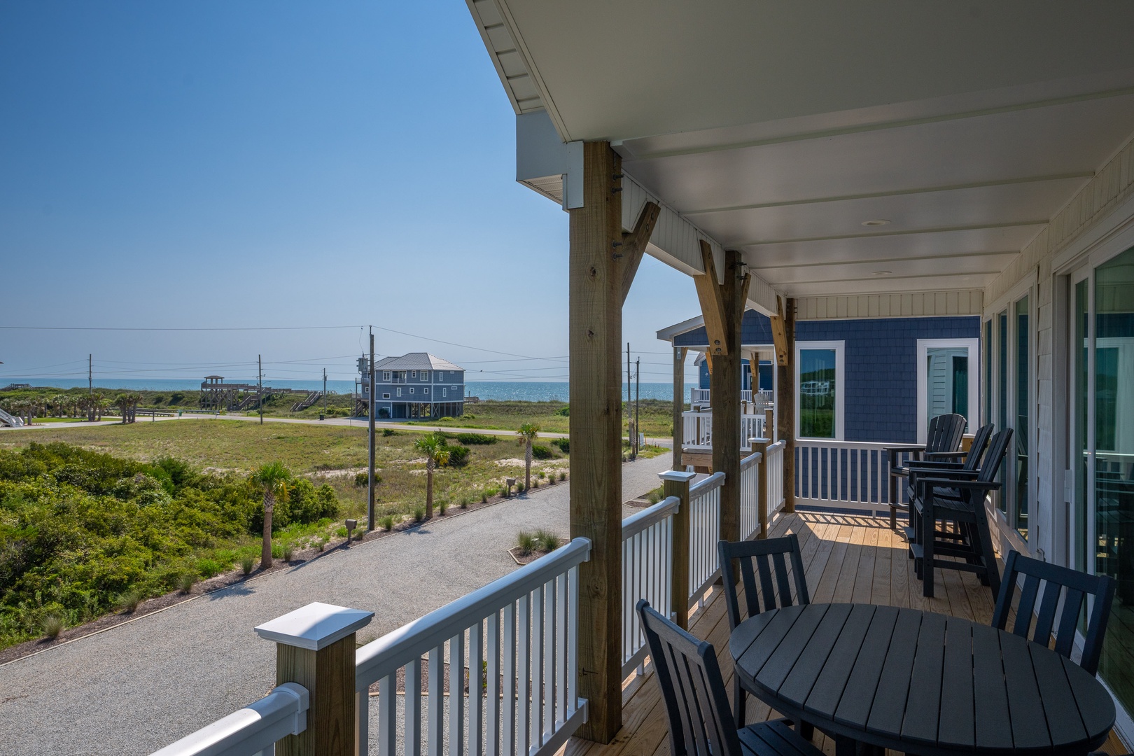 A covered porch overlooking coastal vegetation and the ocean, with seating perfect for enjoying breezy mornings and the rhythmic sound of waves nearby.