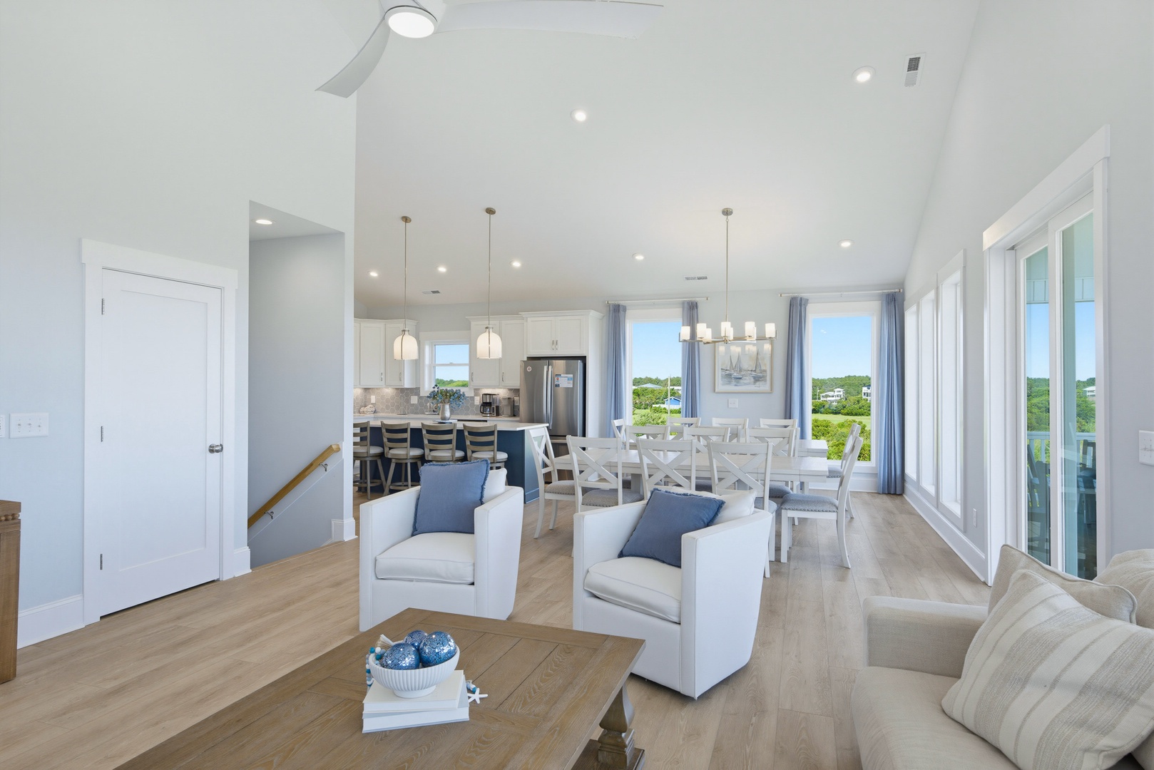 Your open-concept retreat welcomes natural light through floor-to-ceiling windows, framing tranquil green vistas. Coastal-inspired decor creates an airy, inviting atmosphere perfect for unwinding after beach adventures.