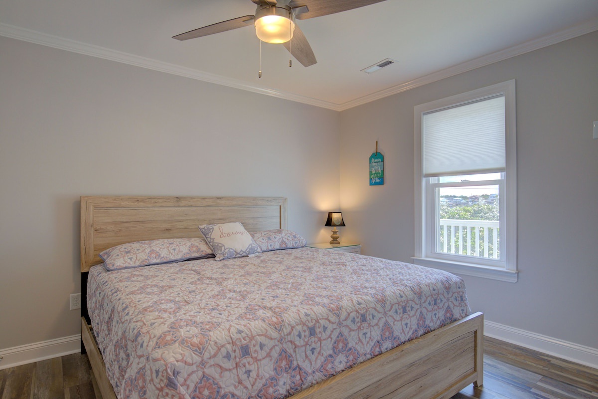 A bedroom with a wooden bed, a ceiling fan, a nightstand with a lamp, and a window with a view.