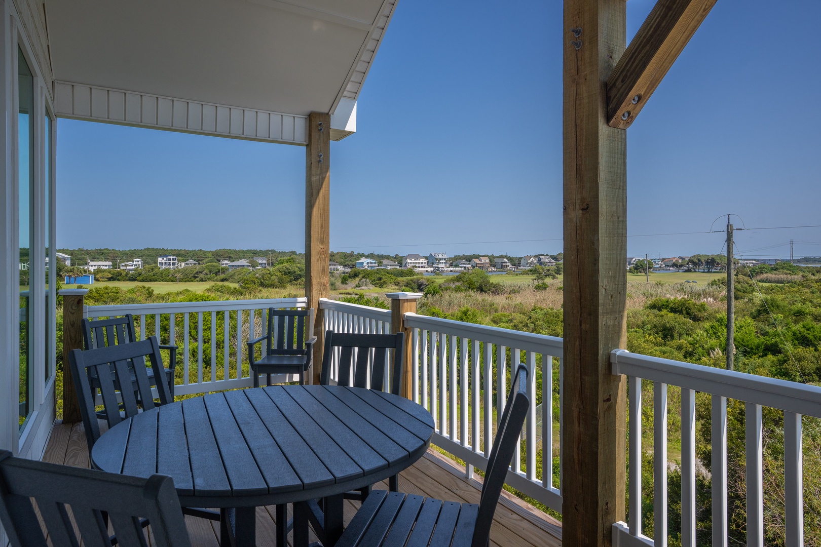 A covered porch offers peaceful views over coastal marshlands and neighboring homes. Relax at your outdoor dining table and let the quiet landscape set the tone for your getaway.