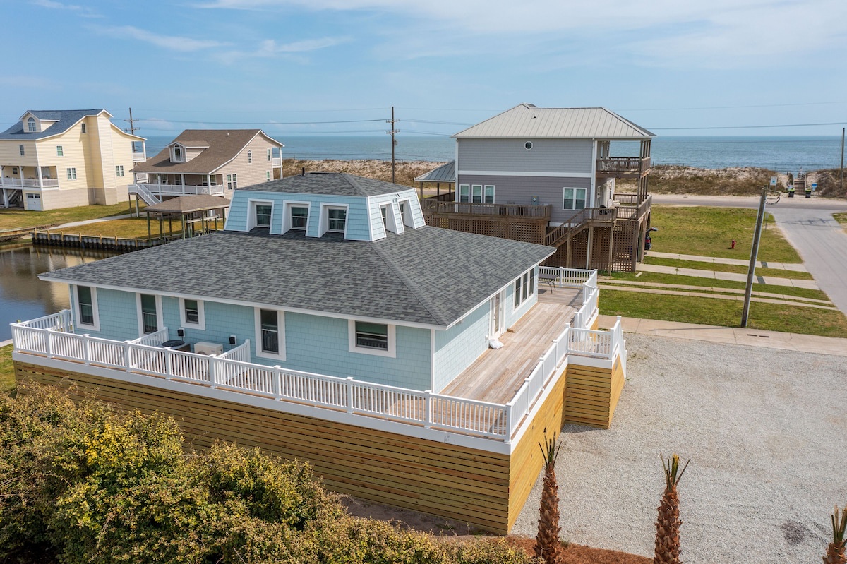 A waterfront property with a large deck, a covered outdoor area, and a view of the ocean.