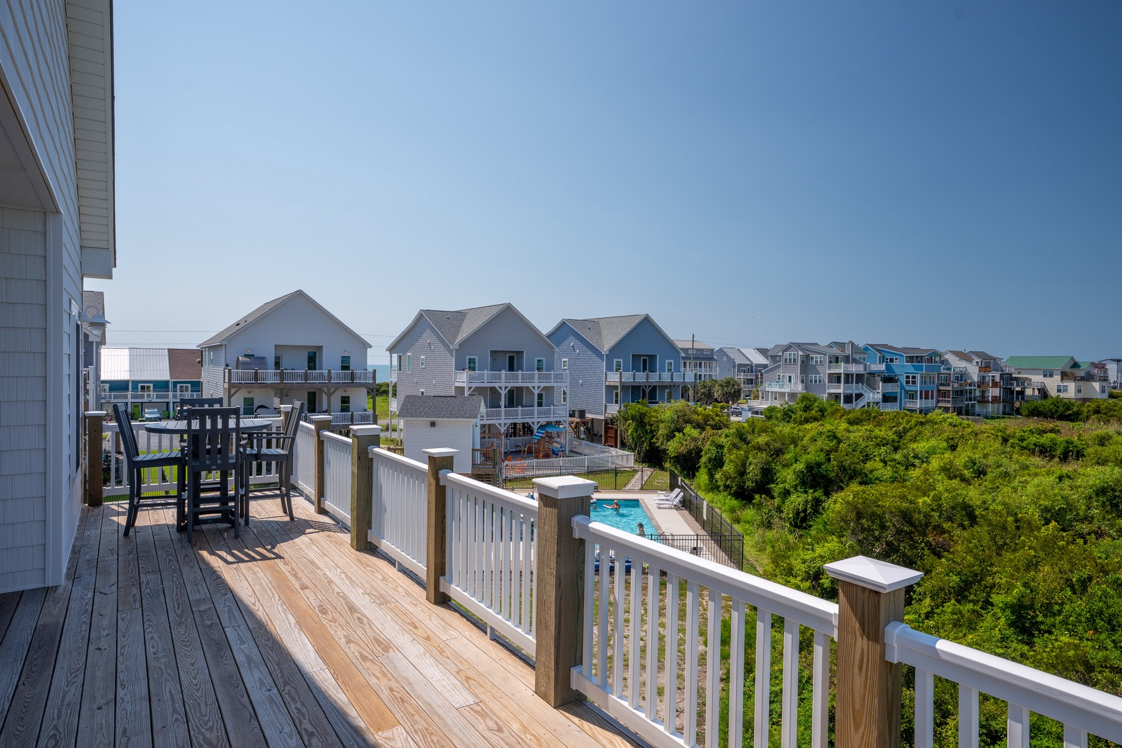 The property sits in a quiet residential coastal neighborhood with nearby beach houses, lush dunes, and a swimming pool visible from the surrounding area.
