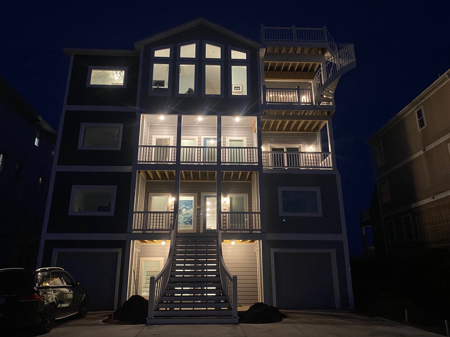 This modern beach home stands tall against the evening sky, showcasing multiple levels of outdoor balconies and spacious rooms designed for your coastal getaway.