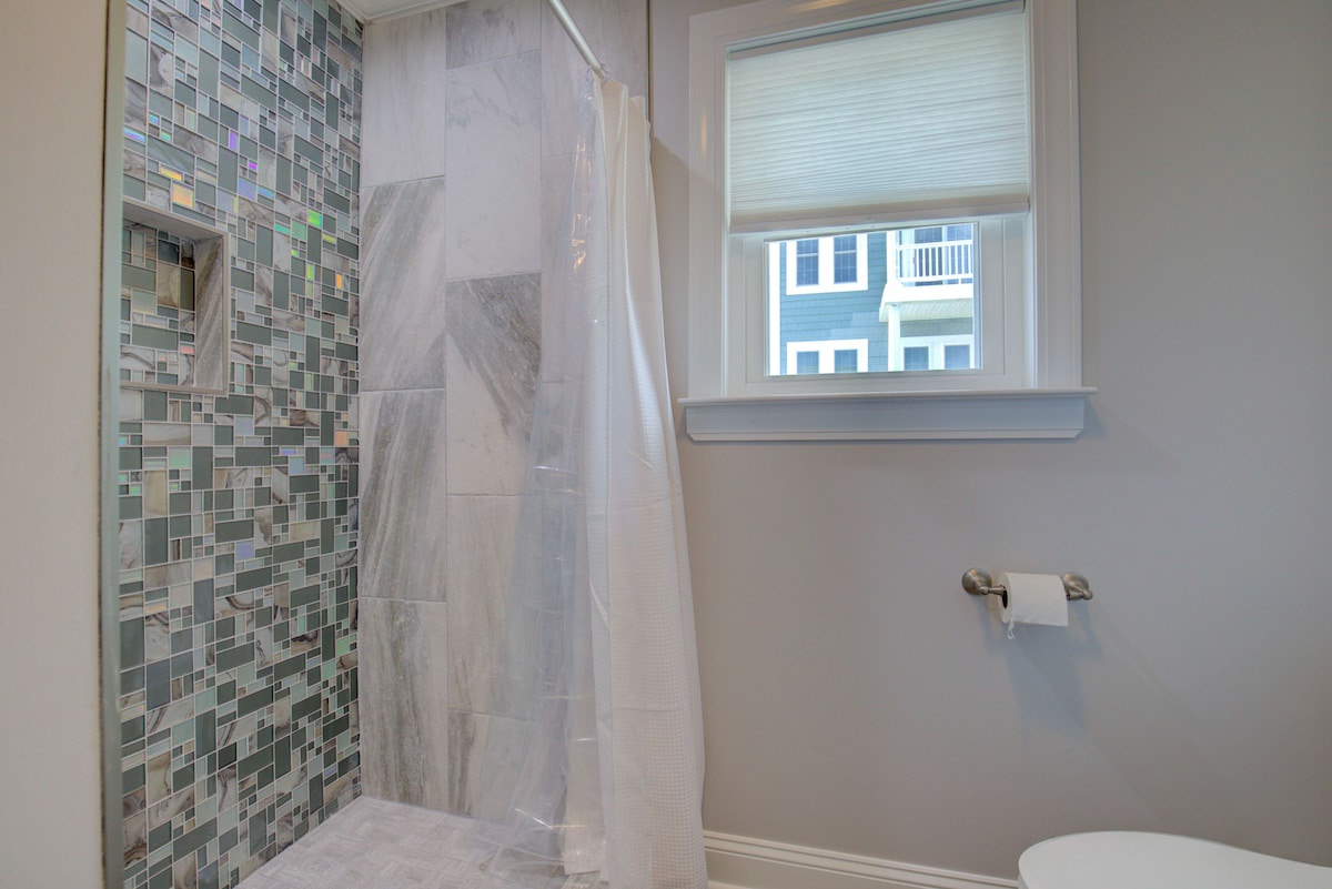 A bathroom with a shower, a window, and a toilet.