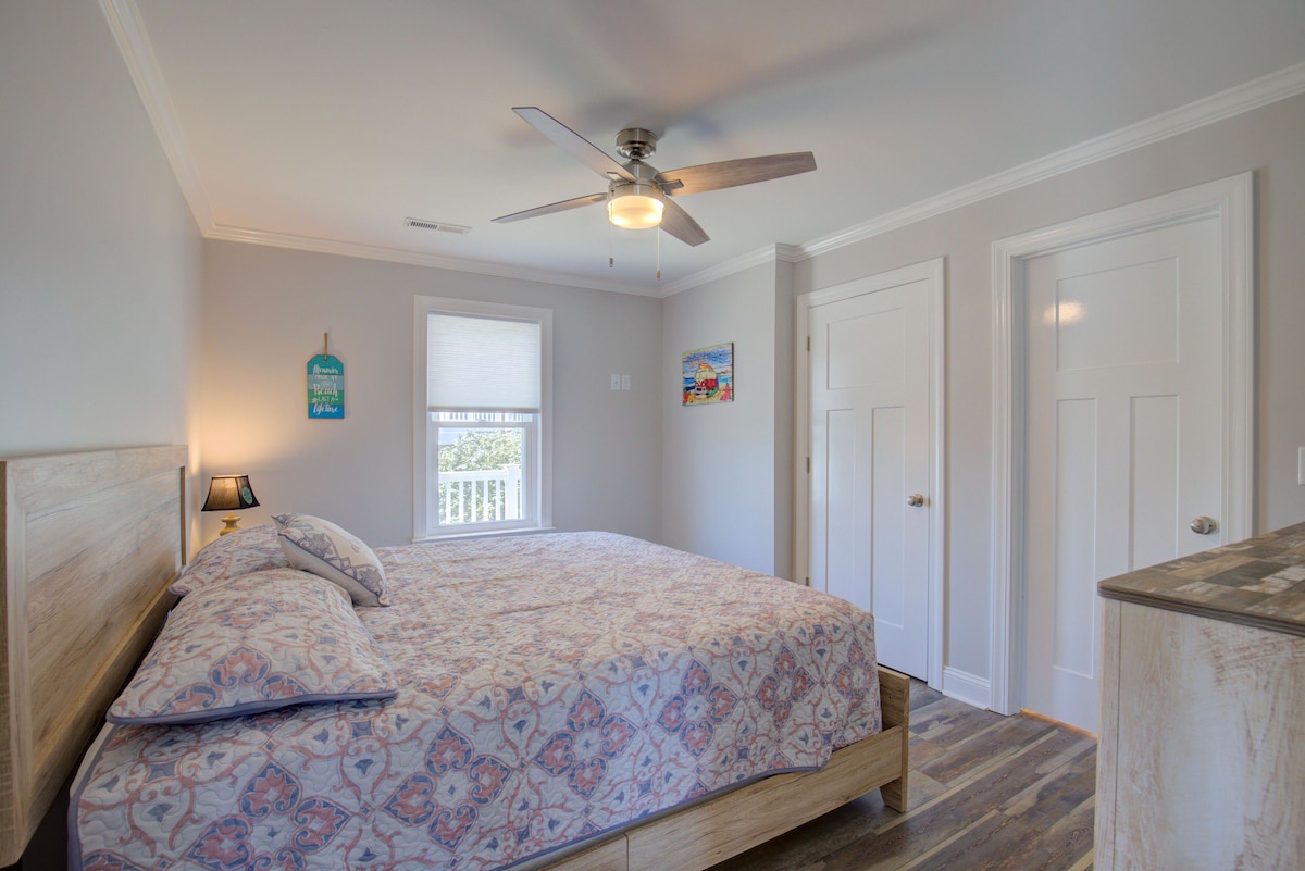 A bedroom with a bed, a ceiling fan, a window, and a door.