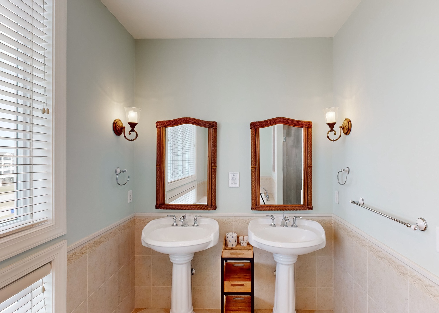 Step into your elegantly appointed bathroom featuring dual pedestal sinks framed by warm wood mirrors and soft sconce lighting—perfect for your morning routine with plenty of space to spread out.