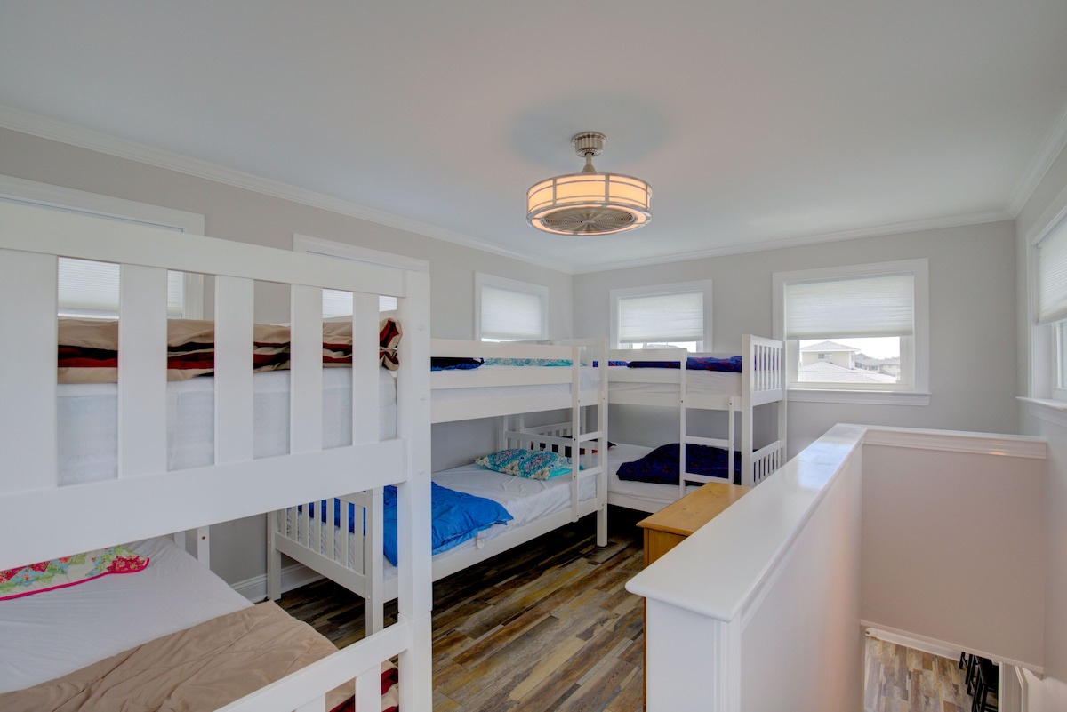 Open loft sleeping area with bunk beds, ceiling fan, and window; this space is not enclosed and is not a private room.