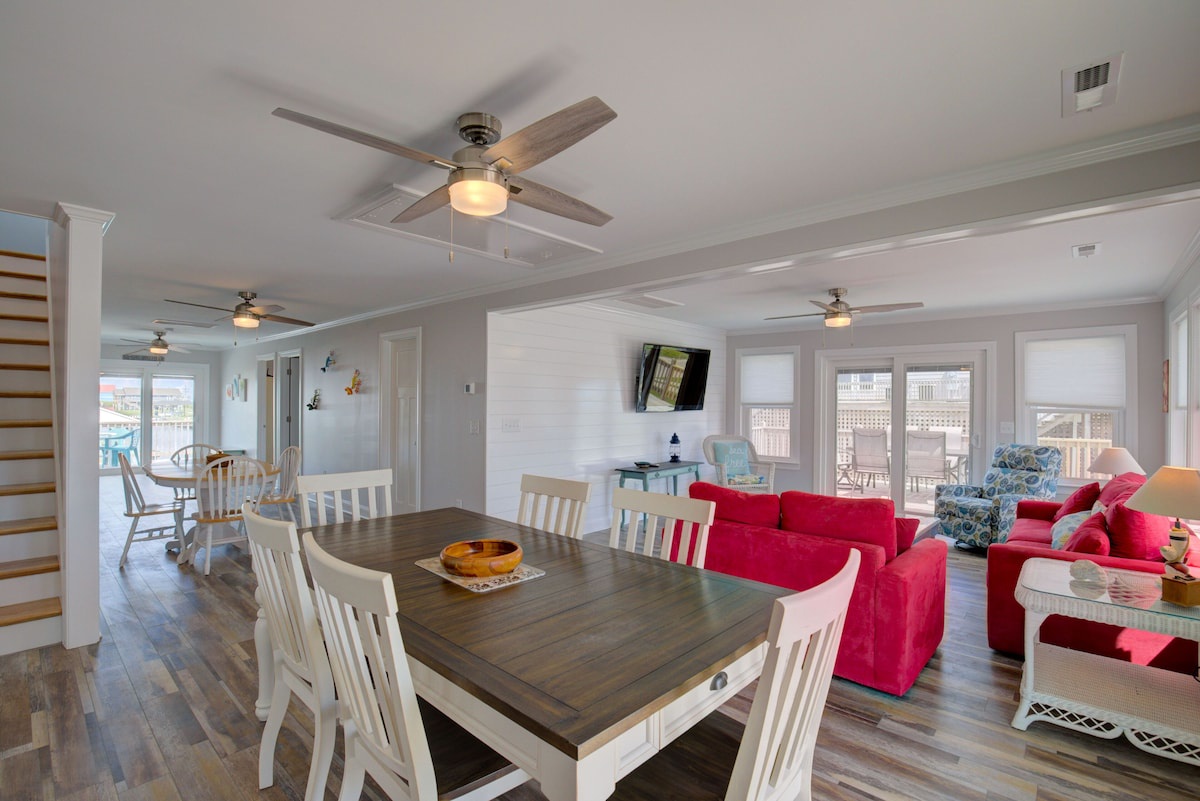 A spacious living area with a wooden dining table, white chairs, a red sofa, and a ceiling fan.